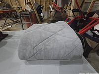 Photo of a folded grey weighted blanket with quilted design on a white table in a workshop setting.