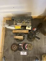 Overview of the lot showing electric jig saw, angle grinder, toolbox with assorted tools, and abrasive discs/wire wheels.