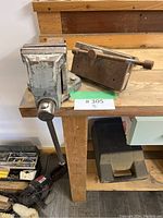 First photo showing two bench vises on a wooden workbench, one positioned upright and one lying on its side, displaying the body and mounting holes.