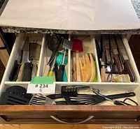 Drawer with a collection of various kitchen utensils including graters, peelers, spatulas, wooden serving forks, and more