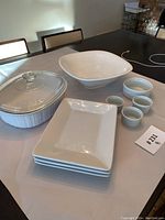 Overview of white Corningware and dishes set including casserole dish with lid, square bowl, rectangular plates, and ramekins.