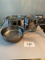 Photo shows all the pots and frying pan on a white surface with lot number 201 visible.