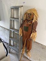 Photo showing a metal step ladder and a fabric scarecrow standing next to it against a white wall.