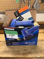 Simoniz cordless orbit polisher packaging box with the polisher showing signs of use, blue color.