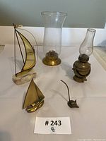 Five vintage brass decorative pieces including sailboats, oil lamp, hurricane glass cover, and brass mouse figurine.