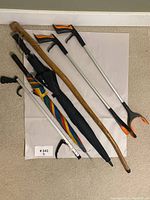 Lot overview showing wooden walking stick, two grabber tools, and two umbrellas arranged on floor.