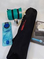 Camping lot with all items arranged including the Game Cot carry bag, Coleman air mattress, water bladder, camp burner bag, and coffee filter.