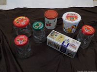 Lot arranged on dark brown cloth, showing all Kraft Bear jars, Cadbury tin, and vintage apple tin.