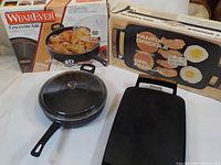 Elegante 5.3 Quart Jumbo Fryer positioned beside its box with glass lid on top; black deep fryer pan with long handle visible.