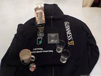 Photo showing all items arranged: black hoodie, black T-shirt, pint glass, two 6oz shot glasses, coffee mug, and glass coaster