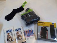 Photo showing entire lot including sealed box of Bench large black t-shirts, an open bag of black crew socks, and three boxes of compression socks from Jobst and Sigvaris.