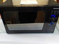 Front view of Panasonic microwave showing black glass window and digital display showing 'PRESS P10'.