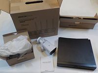 Photo showing a DragonTouch DVR unit, one security camera, quick start guide and packaging boxes.