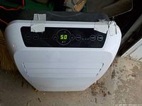 Top view of white portable air conditioner showing control panel with digital temperature display and tape on sides.