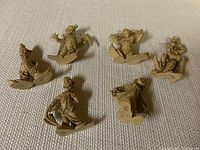 Photo showing a group of six vintage small clown figurines arranged on a textured surface. Figurines are cream-colored, each in unique playful poses.