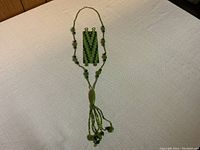 Green beaded necklace and matching woven bracelet laid out on neutral fabric background.