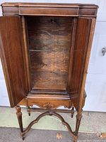 Inside view of the cabinet with doors open revealing wooden interior with a single glass shelf and visible light fixture inside at top.