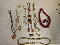Photo capturing six pieces of costume jewelry including necklaces made of various beads and chains and one pair of clip-on earrings.