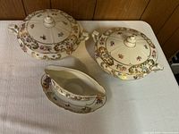 Two covered porcelain bowls with lids and a gravy boat with matching plate, decorated in ornate floral Dresden style.
