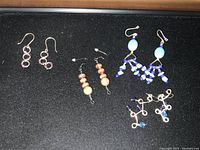 Four pairs of handmade earrings displayed on black fabric background with gold frame around.