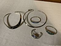 Photo showing five pieces of sterling silver jewelry including two choker necklaces and three cuff bracelets with colorful inlays