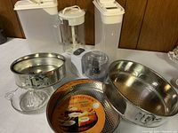 Overview of kitchen lot including baking pans, food containers, juicer, and mini chopper