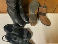 Three pairs of ladies shoes and boots including black tall boots, tan ankle boots, and black wedge sandals with elastic straps.
