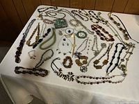 Wide angle view of large assortment of costume jewelry spread on a white tablecloth showing variety of necklaces and bracelets.