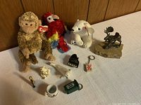Overview of toys and miniatures including two plush toys and assorted figurines spread on a white towel