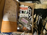 Box containing assorted craft supplies, including small bottles, dried herbs, and instructions.