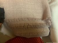 Folded beige textured fabric with fringed edges, showing texture and color.