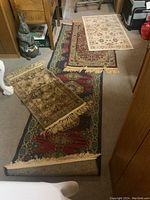 Photo shows five rugs laid out: one large runner with red and blue geometric floral patterns, four smaller mats in various colors and designs, some fringed edges visible.