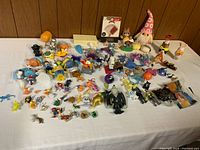Wide view of the assorted toy collection laid out on a flat surface, showing numerous cartoon and fantasy figures including Smurfs and animals.