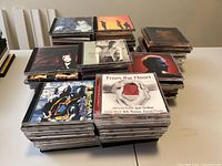 Stacks of over 80 jewel case CDs arranged in multiple piles on a table, showing various artists and genres.