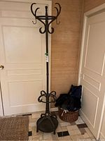 Full view of the metal coat tree placed indoors showing the entire structure including base, pole, and hooks.