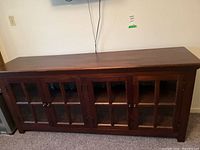 Front view of dark wood credenza with four glass inset doors and metal knobs.