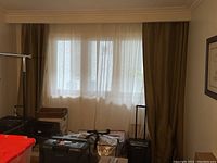 Window with two brown Restoration Hardware drapes hung on a curtain rod, partially covering sheer curtains and surrounded by wall and furniture.