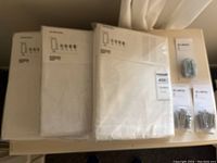 Three new in package IKEA Silverlonn drapes and three packages of Riktig hooks displayed on a surface.