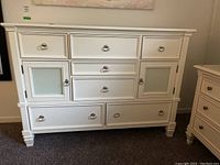 Front view of white wood dresser showing nine drawers and two frosted glass cabinet doors and silver ring pulls