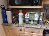 Full view of lot items on counter including bottles, tumblers, Yeti bag, and thermos jars