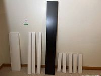 Ten IKEA wall mount shelving units in a group displayed vertically along a wall in a basement, with white and one black shelves of varying sizes.