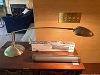 Photo showing metal table lamp with adjustable arm, dome shade, round weighted base, and the LP-S08 soundbar with its original box behind it.