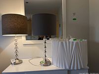 Two matching 28-inch high table lamps with dark fabric drum shades and silver bases with clear glass sphere accents next to a white pleated ceiling lamp.