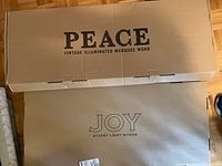Boxes labeled "PEACE VINTAGE ILLUMINATED MARQUEE WORD" and "JOY STARRY LIGHT WORDS" with size details on cardboard boxes.