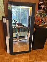 Full view of the large framed mirror standing upright, reflecting room interior and furniture.