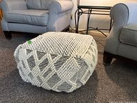 Photo showing textured fabric ottoman with looped black and cream geometric pattern, placed on carpet.