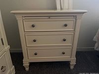Front view of white 3 drawer side table with metal round knobs and carved details.