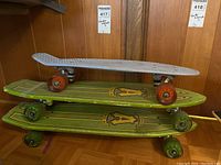 Three skateboards stacked horizontally against wooden panel walls, two larger Airwalk boards with green decks on bottom and one smaller gray deck skateboard on top