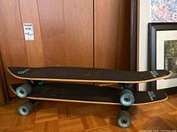 Two stacked Quest Super Cruiser Remix skateboards showing deck sizes and side profile with teal wheels.