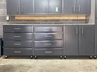 Front view of all three grey garage storage cabinets showing drawers, cupboard doors, and stone countertops.